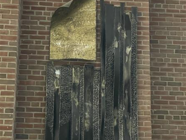 The metal flag sculpture on display against the brick of the auditorium